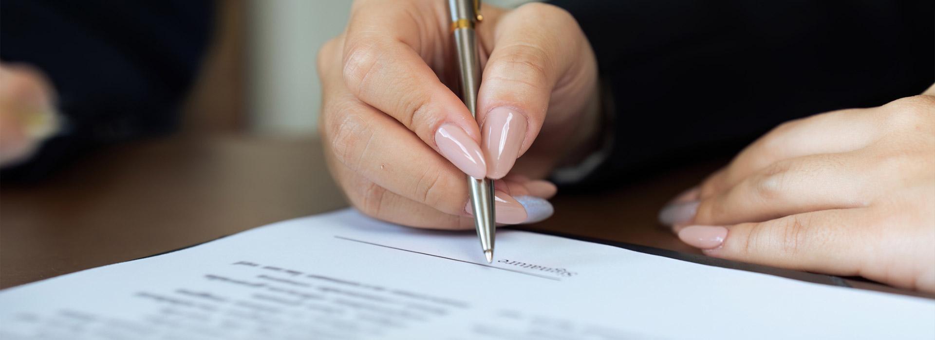 lady's hand holding pen and signing paper