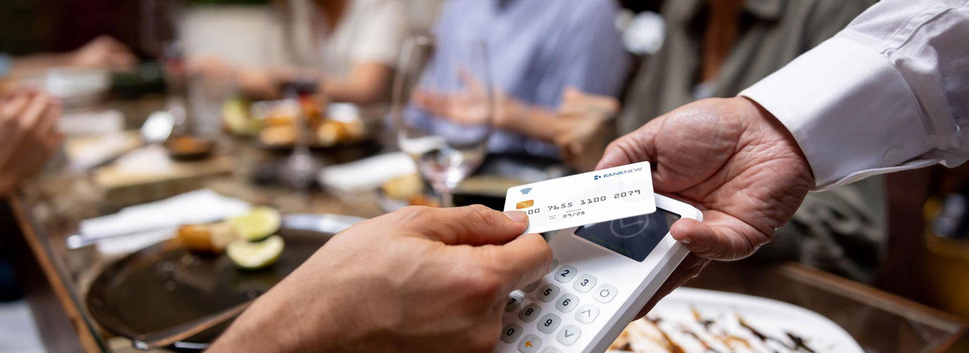 people at dinner table and hand tapping credit card to pay bill