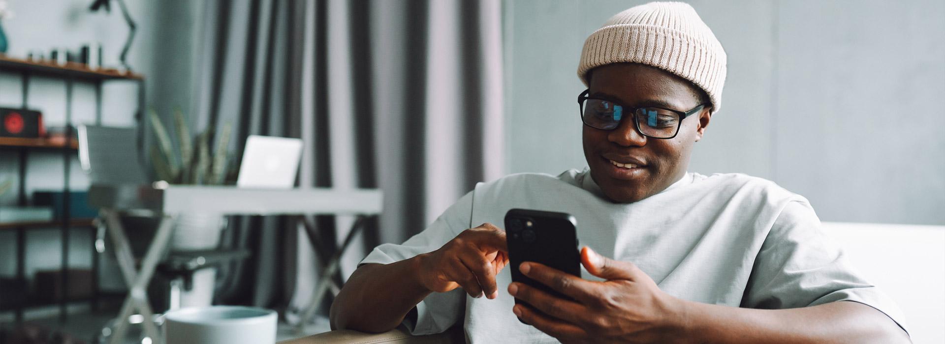 Black man with ski hat on holding cell phone in hand making a transaction