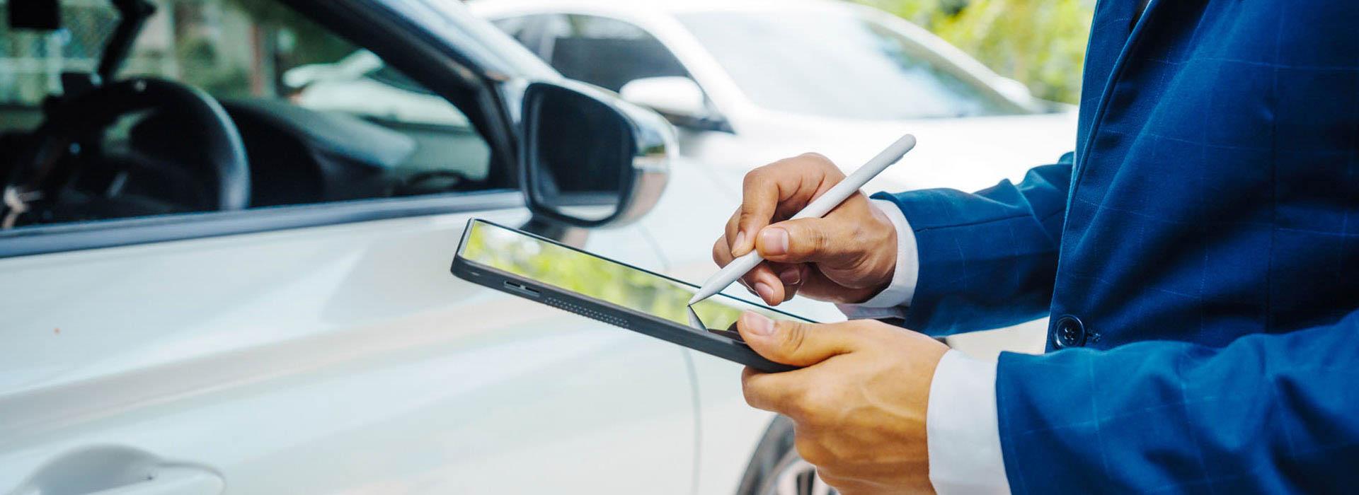 guy signing name on a computer tablet in front of a car
